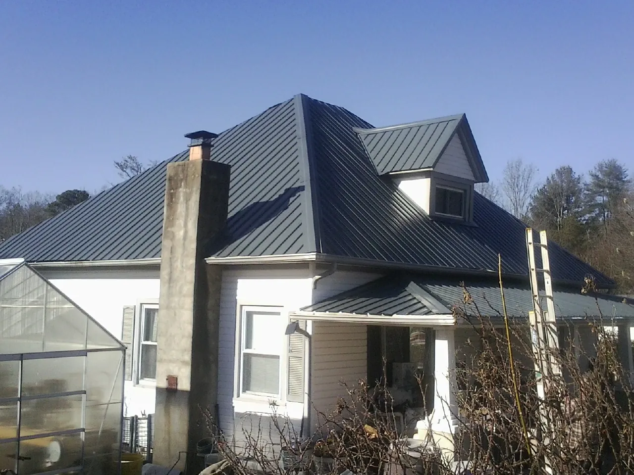 Dark blue standing seam metal roof on a white farmhouse with dormer — Slate & Tile Roof Repair by Roofing Brothers in Corbin