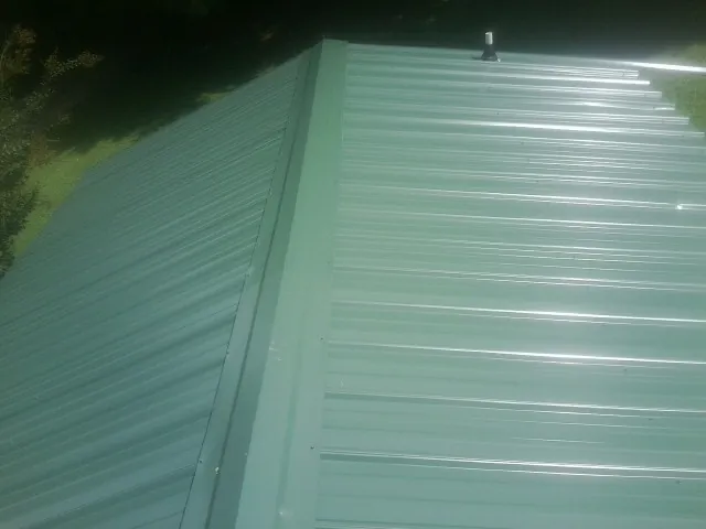 New green metal panels meeting at the ridge of a roof — Flat Roof Repair work by our crew in Corbin