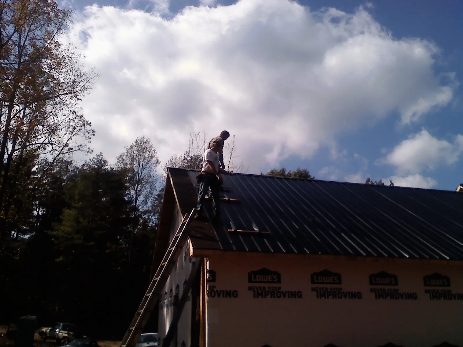 Roofer fastening dark metal panels high against a cloudy sky, from a Roof Inspection job in Corbin