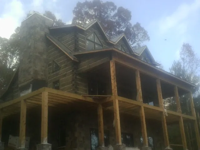 Stone chimney and dormers on a large log home with a timber porch in Corbin